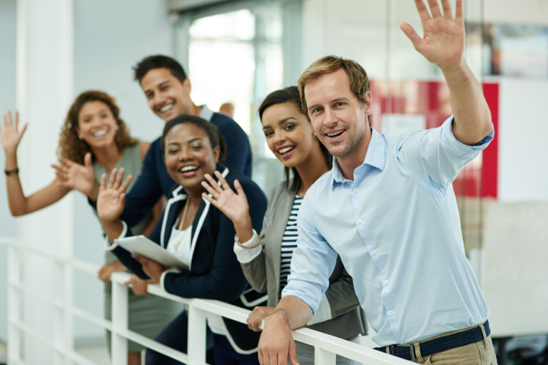 group of people indoors, all smiling and raising their hands.